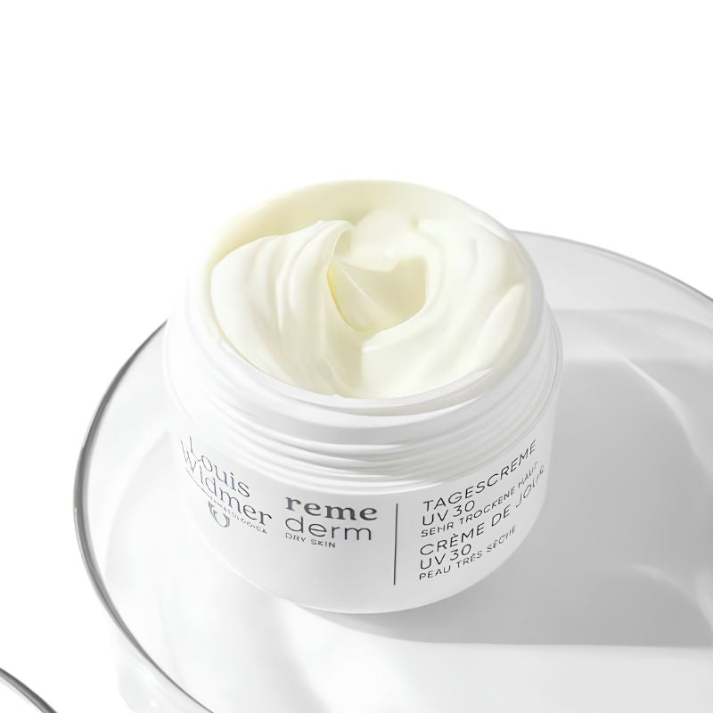 A white cosmetic jar of Yves Saint Laurent Reme Tagescreme moisturizer, filled with thick white cream and resting on a clear glass plate against a white background.