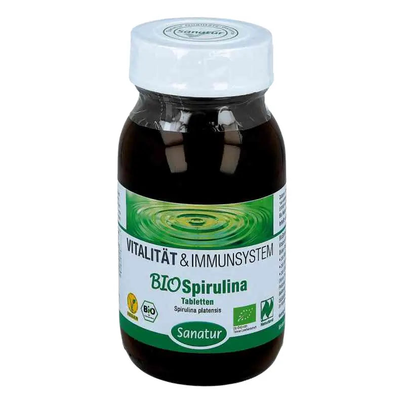 A bottle of Sanatur Bio Spirulina tablets, featuring a dark brown bottle, a white cap, and a green and white label with a water ripple design.