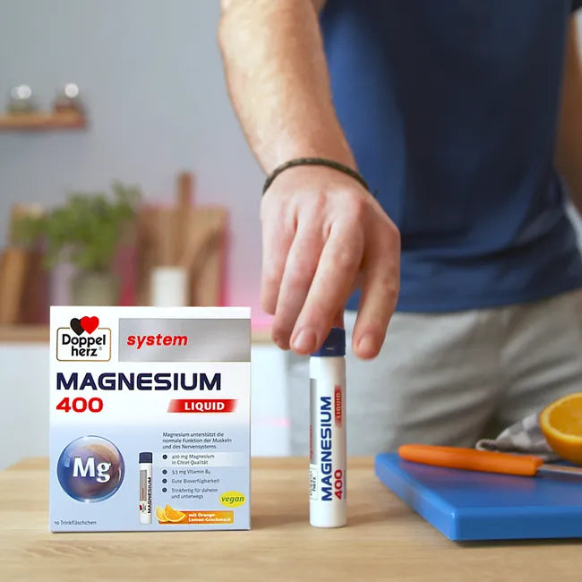 Lifestyle photo showing the Doppelherz Magnesium package on the kitchen countertop. One phial has been taken out of the box. A man stands behind the countertop and is about to take and drink the phial.