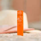 Orange Avene lip balm packaging on a blurred natural background